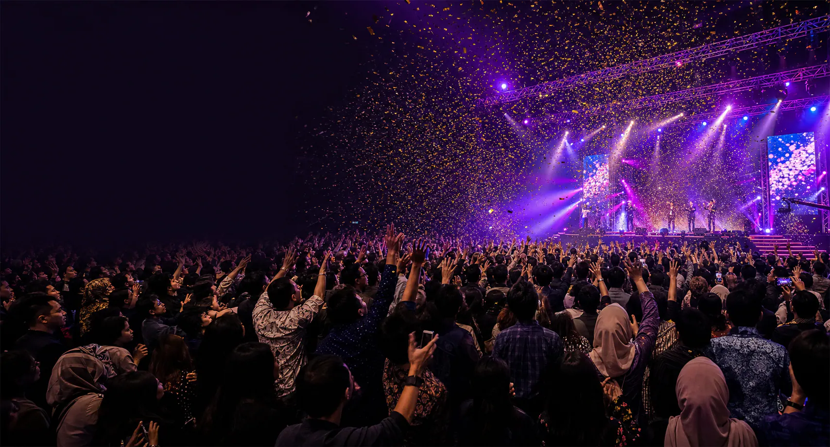 Corporate audience celebrating beneath purple stage lights and gold confetti